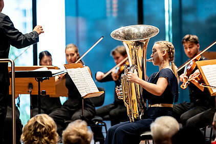 Eine Frau spielt Tuba zusammen mit mehreren Streicher*innen vor Publikum