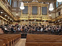 Orchester bei einer Probe in einem historischen Wiener Konzertsaal, umgeben von reich verzierten Emporen und Balkonen.