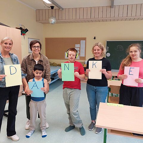 Eine Gruppe von Lehrerinnen und Schülern der Allgemeinen Sonderschule Hopfgarten halten bunte A4-Blätter mit den Buchstaben DANKE - also Danke in die Kamera