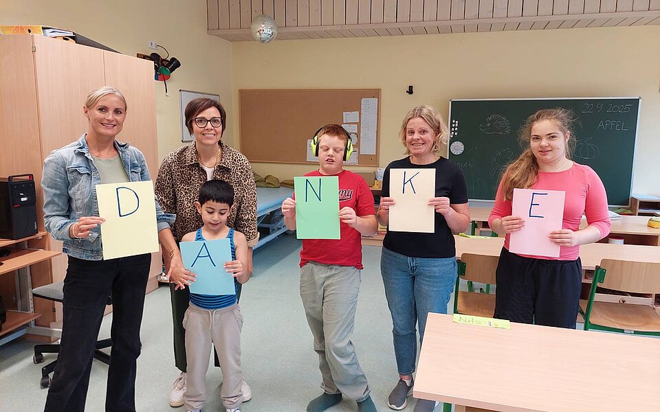 Eine Gruppe von Lehrerinnen und Schülern der Allgemeinen Sonderschule Hopfgarten halten bunte A4-Blätter mit den Buchstaben DANKE - also Danke in die Kamera