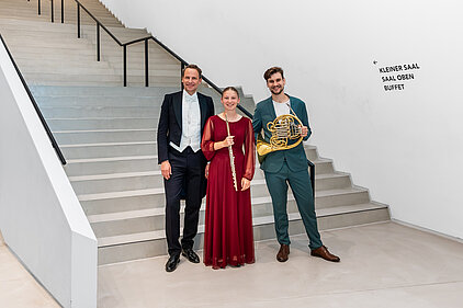 Der Dirigent steht mit der Solistin und dem Solisten auf einer Treppe 