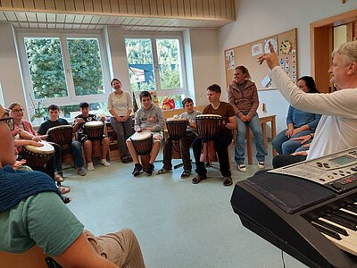 Eine große Gruppe von Schülern und Betreuern mit dem Gesangspädagogen Martin Spöck in voller Aktion beim Trommeln