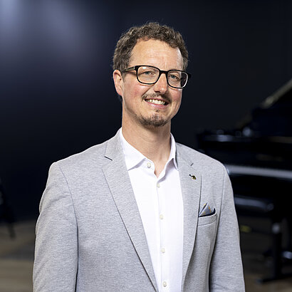 Portrait von Musikschuldirektor Christian Schönegger in grauem Sakko vor einem schwarzen Klavier